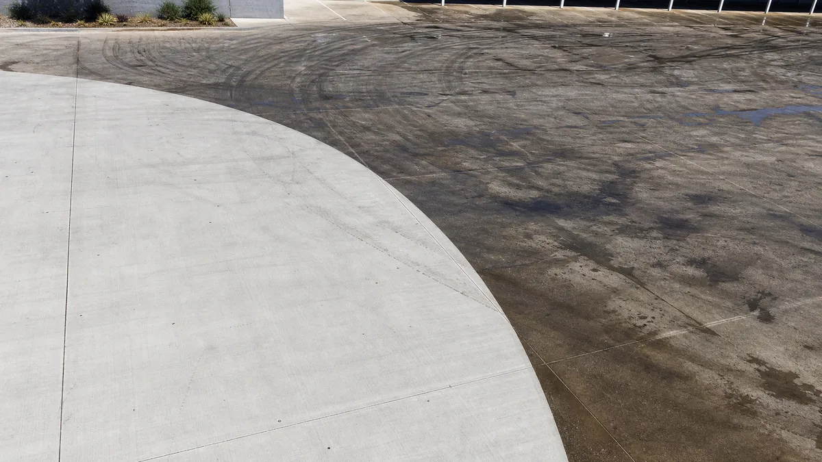 Wide commercial carpark being high-pressure cleaned, clean arc through tyre marks and grime