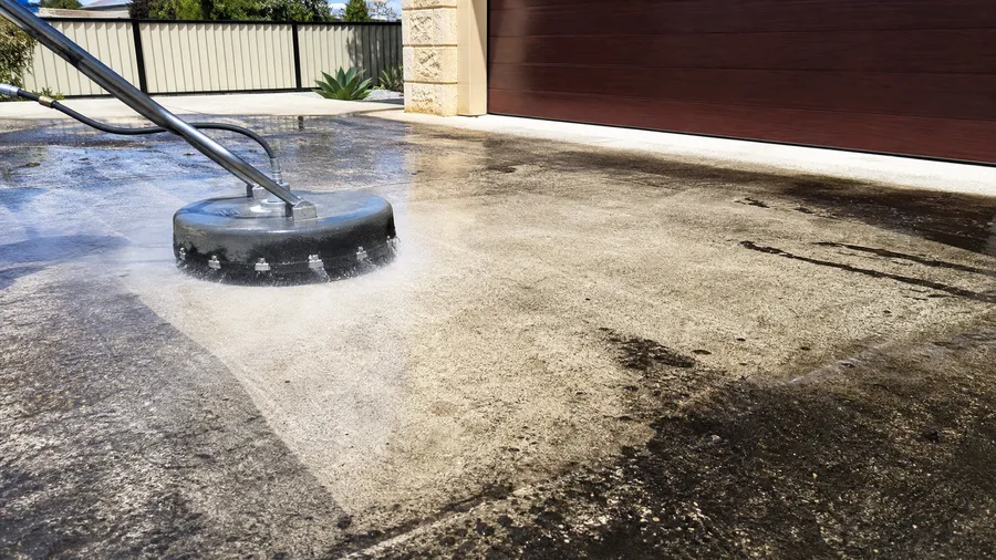 Rotary surface cleaner blasting black mould from a concrete driveway
